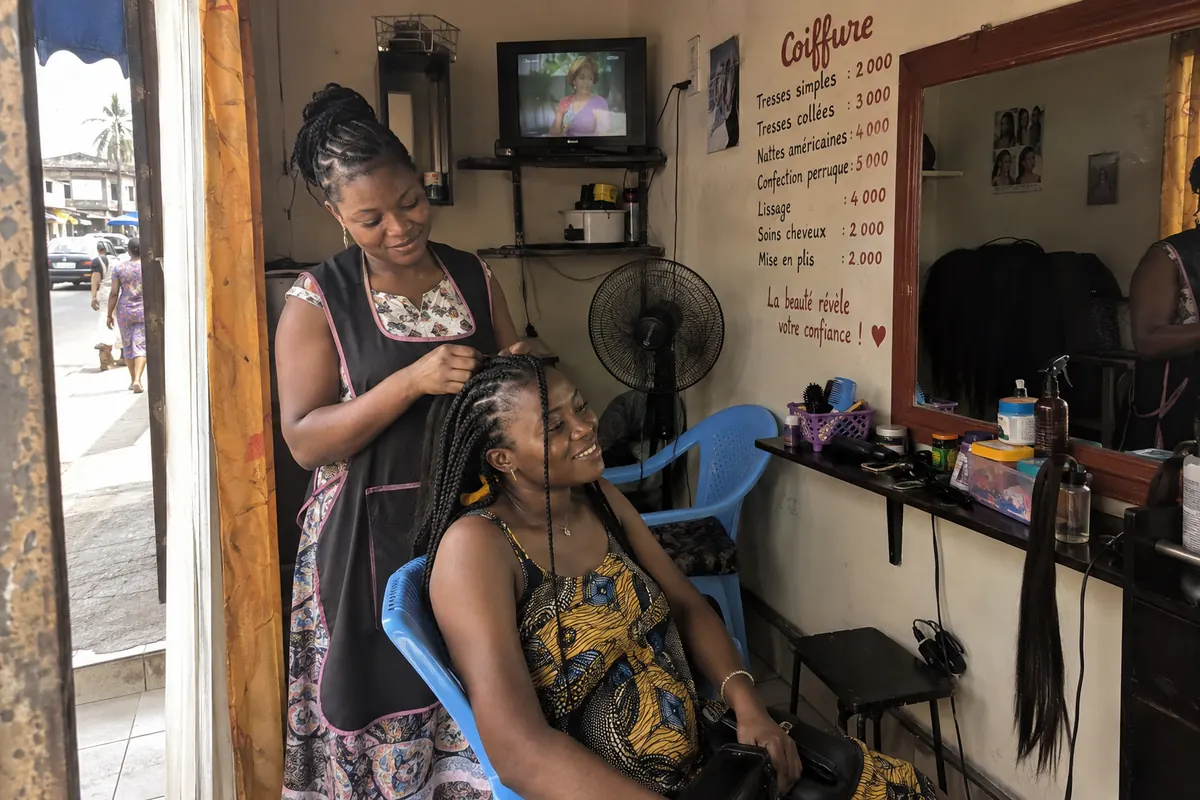 Une coiffeuse tresse les cheveux d’une cliente dans son salon